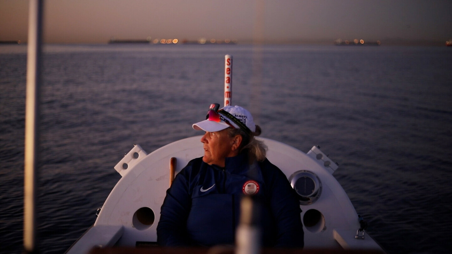 Frau in Sportkleidung sitzt auf einem Ruderboot bei Dämmerung, mit Blick auf das ruhige Wasser.